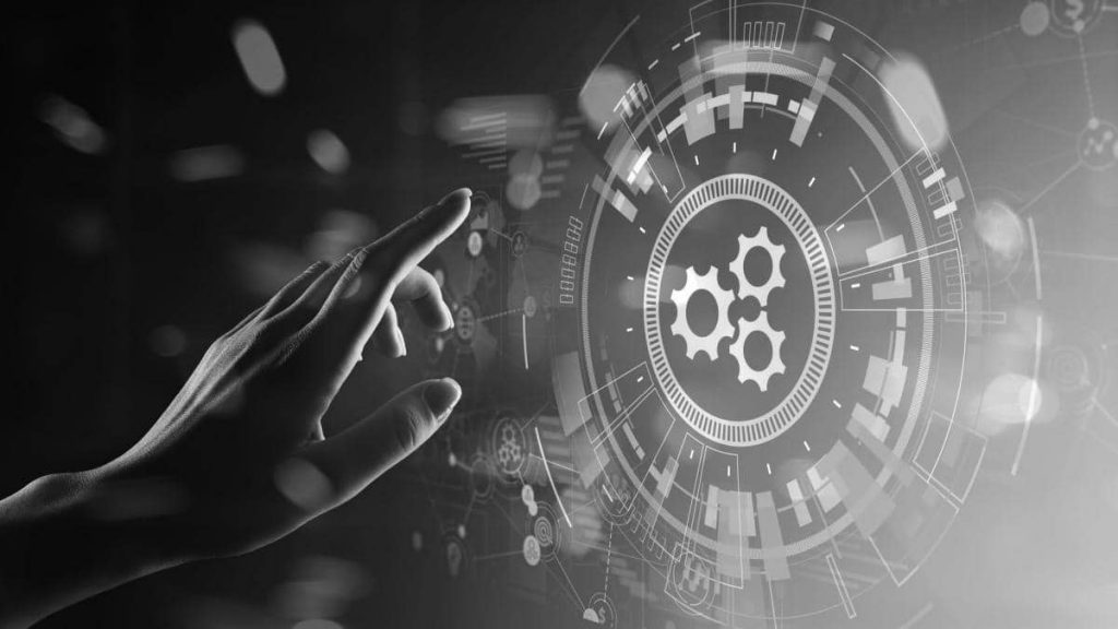 A black and white image of a woman's hand reaching for a holographic image of a 3 cogs in concentric circles.